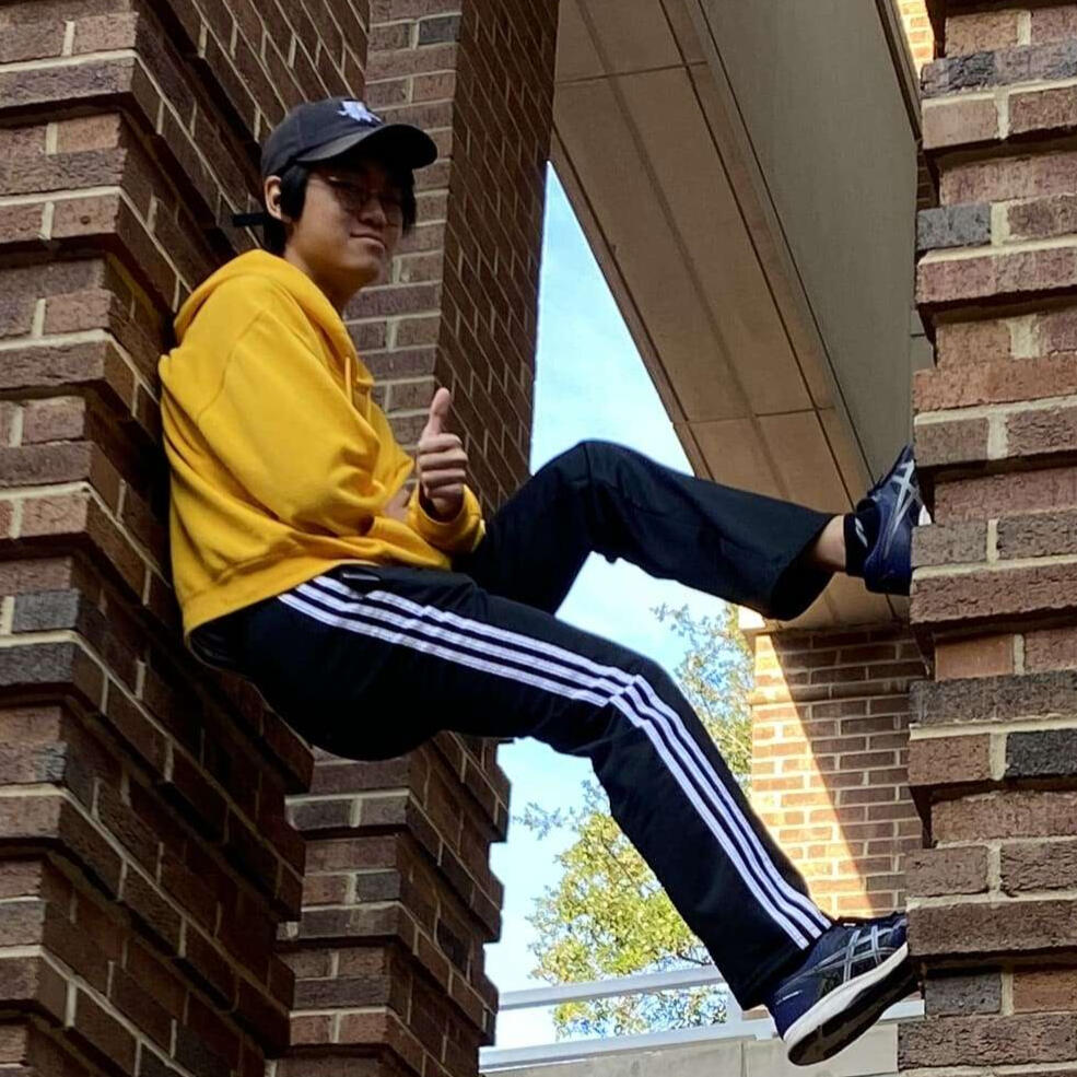 A photo of Joshua Loo standing between two brick pillars